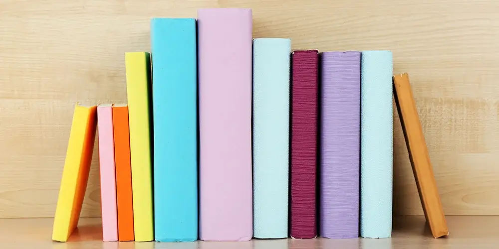 Monwell case study - Row of colorful, unlabeled books in various pastel shades standing on a light wood shelf.